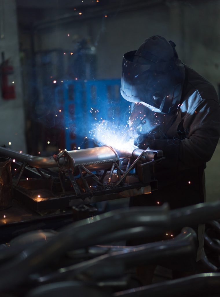 worker-welding-exhaust-pipes-pieces-together.jpg